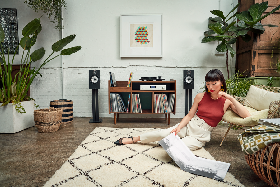 A woman sits on a rug on the floor while she enjoys an LP record from Bowers & Wilkins speakers. 