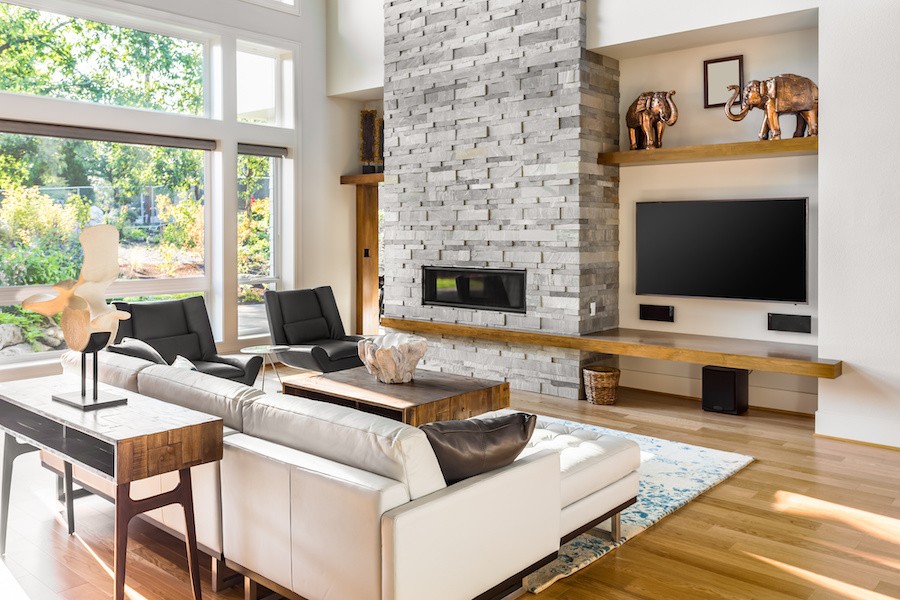 A well-lit home with a couch, rolled-up motorized shades, and a wall-mounted TV. 