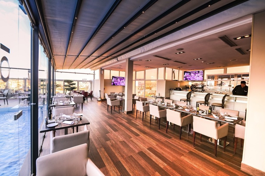 A rooftop restaurant with a view and glass windows overlooking the outdoor dining area.