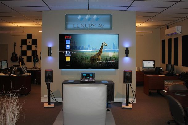 Demo area with Luxury AV sign, TV display, and speaker setup